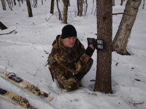 a man croached in the snow fitting a camera trap in the snow. Gifts for big cats
